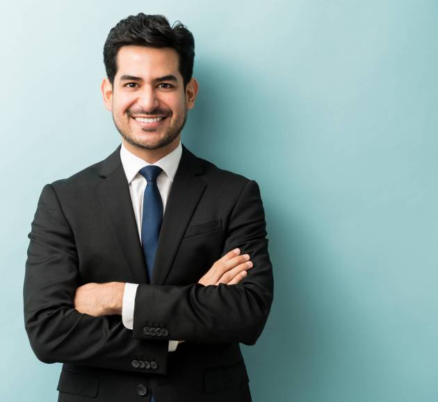 smiling-young-male-professional-standing-with-arms-crossed-while-making-eye-contact-against-isolated-background-min